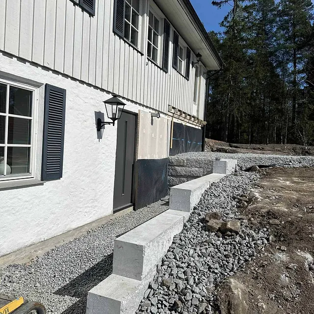 Nye betongblokker lagt som mur langs vegg på hvitt hus.