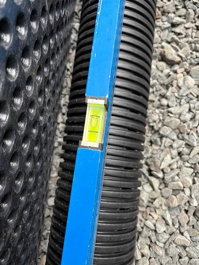 Vater ligger på drensrør ved knotteplast og pukk, brukt for nøyaktig justering av fall.