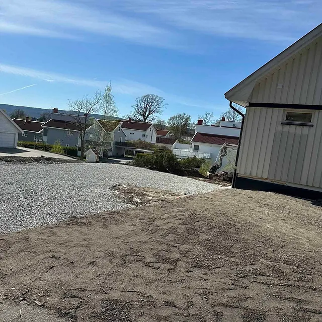 Nivellert tomt med jord og grus utenfor hvitt hus i boligfelt.