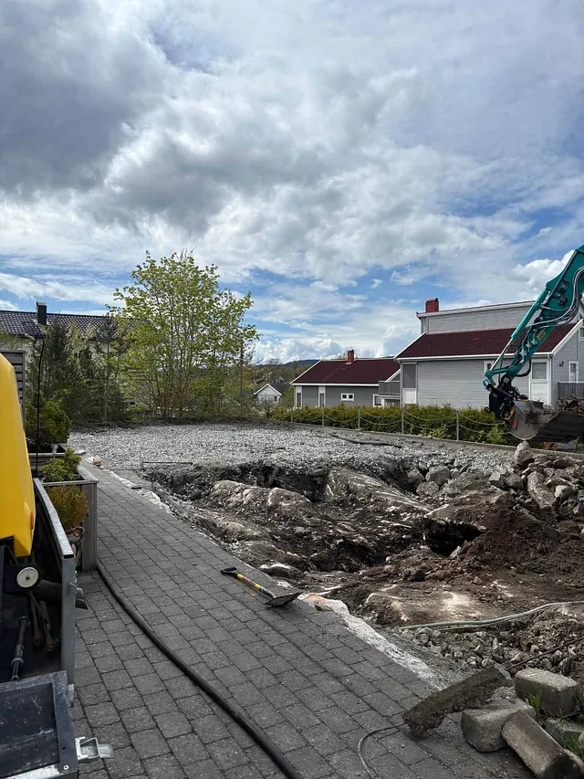 Tomt klargjort med sprengt fjell og grus ved boligområde, med maskin og verktøy langs kant.